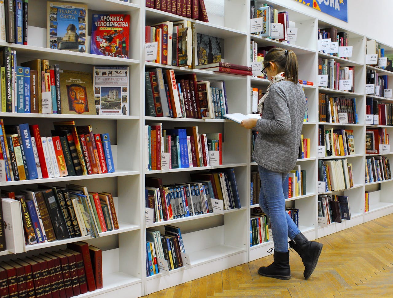 creative-02 A young woman stands reading a book in a well-stocked library.