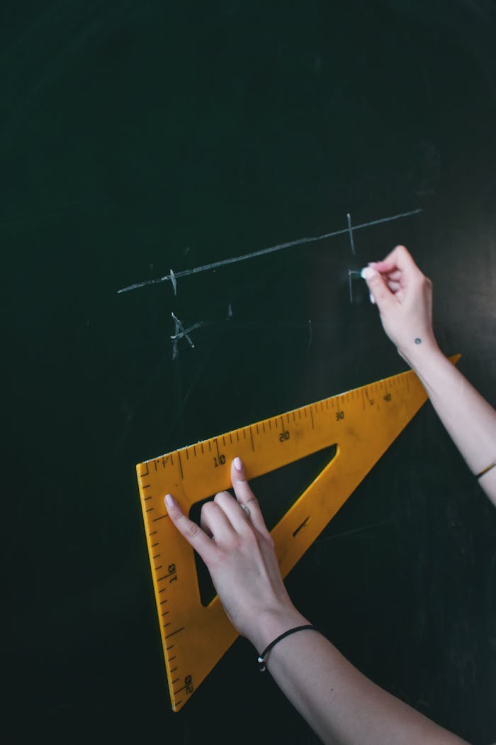 Services-02 Two hands drawing a line with chalk on a blackboard using a triangle ruler