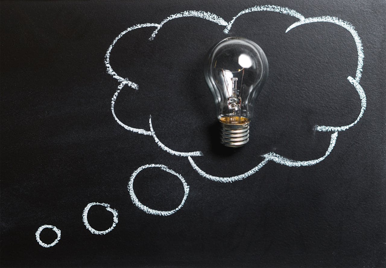 brand-02 Light bulb laying on chalkboard with drawn thought bubble, symbolizing creative ideas.