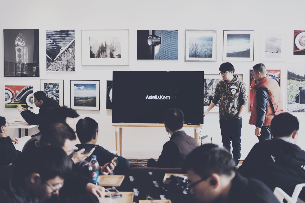 why-choose-us A group of adults attending a casual business presentation in a modern art space, featuring a TV display and framed art.